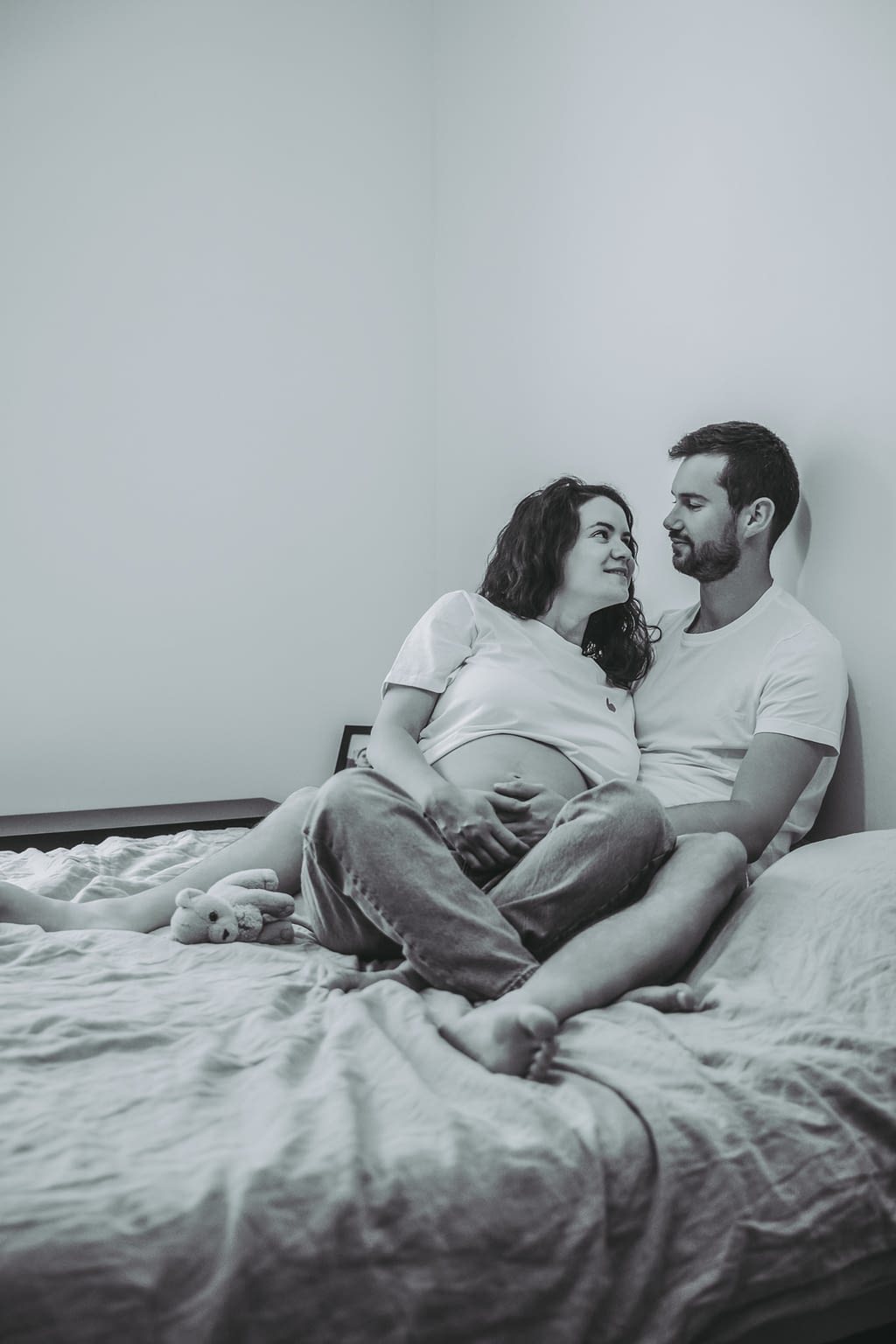 Photographie d'un couple assis avec femme enceinte dans un lit qui se prennent dans les bras
