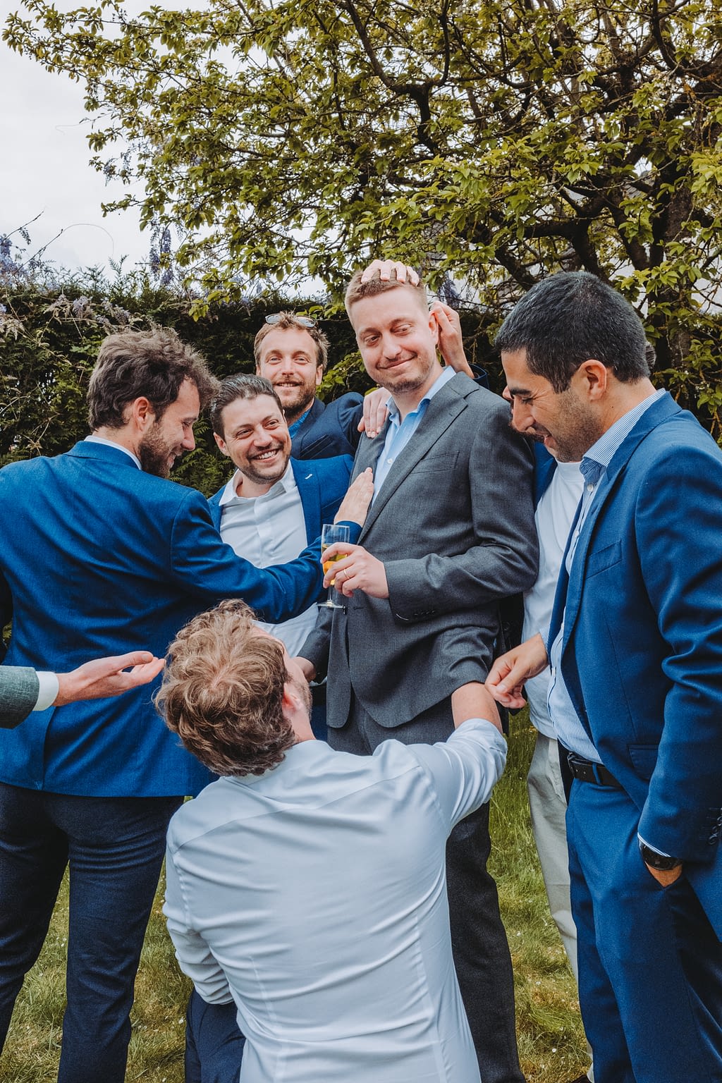 Photographie de mariage d'un groupe de copains avec le marié en train de lui toucher ses vêtements et sa tête