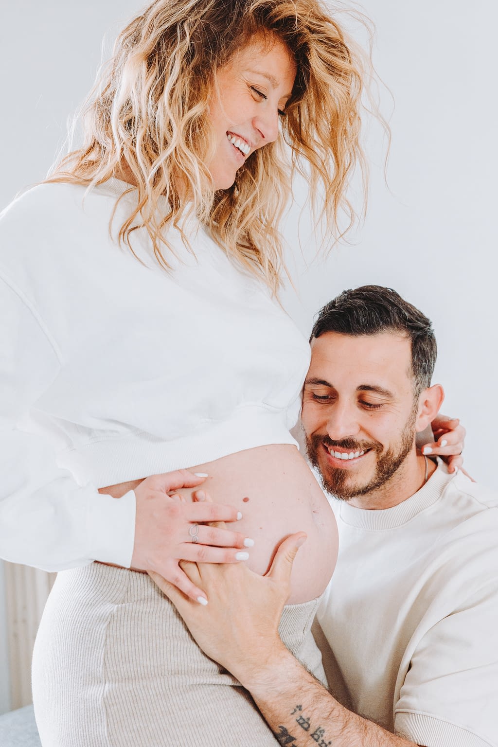 Photographie d'un jeune couple avec femme enceinte. Le papa tient le ventre de la maman qui rigole.