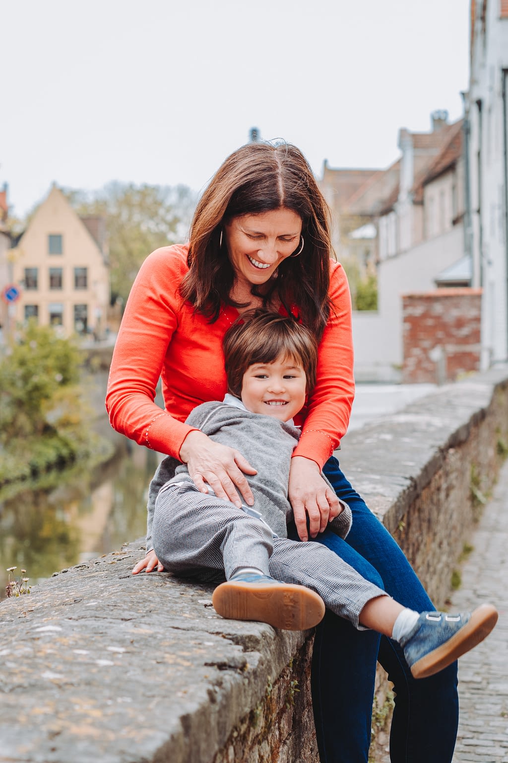 Photographie d'une maman et son petit garçon assis sur le rebord d'un canal dans la ville de Bruges