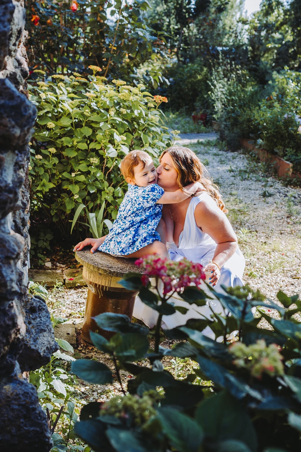 Photographie de la mariée qui fait un baiser à sa fille dans un jardin