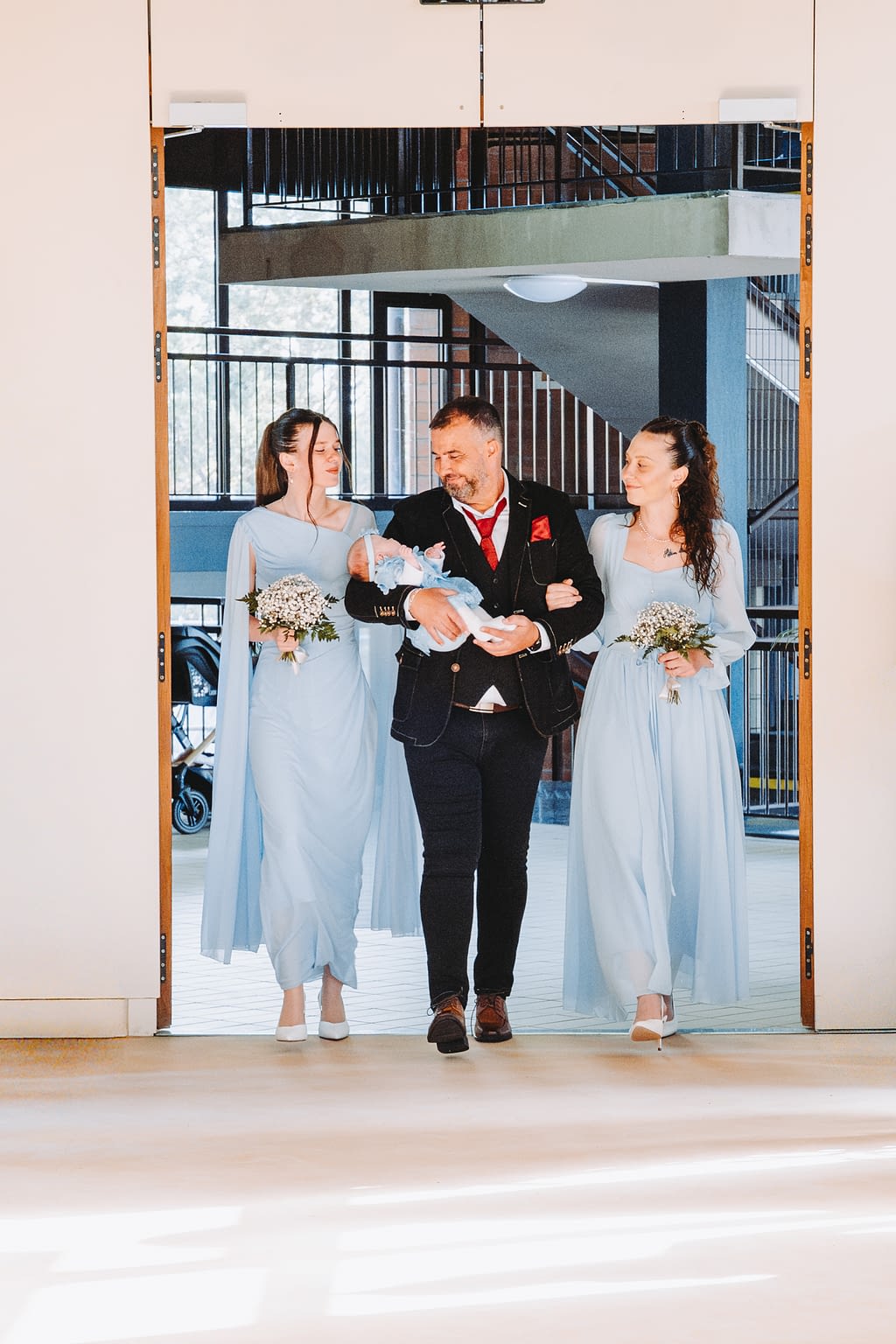 Photographie d'un marié qui entre dans la mairie accompagné par ses 2 filles et portant son dernier enfant dans les bras