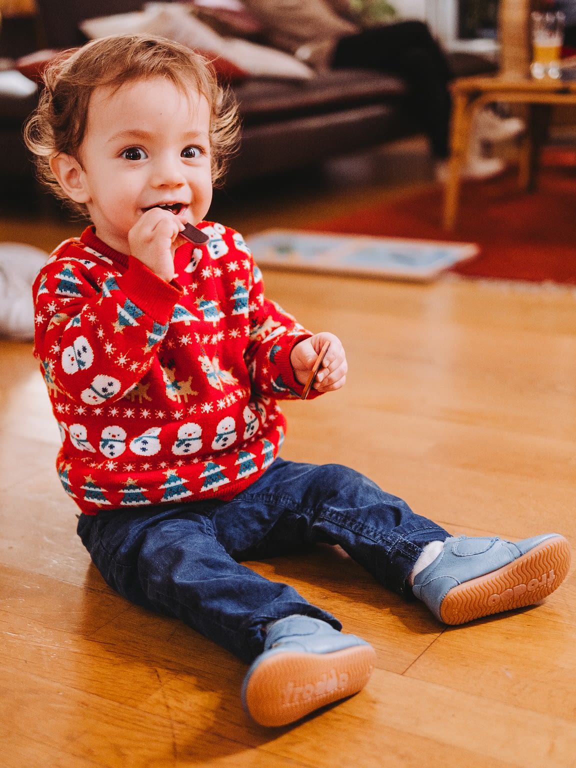 Petit garçon en pull de Noël assis par terre qui machouille un jouet