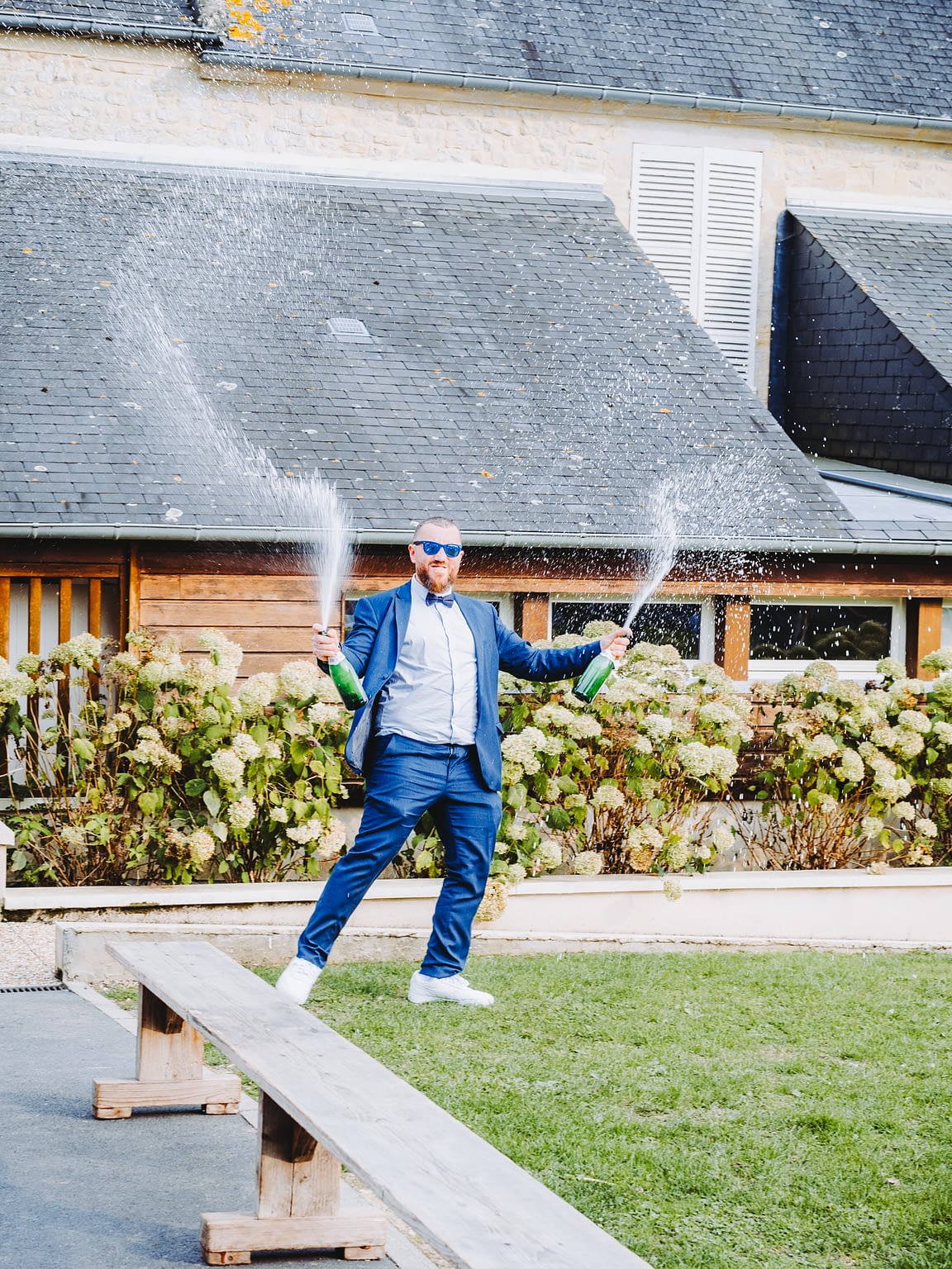 Photographie d'un marié avec 2 bouteilles de champagne qui explosent