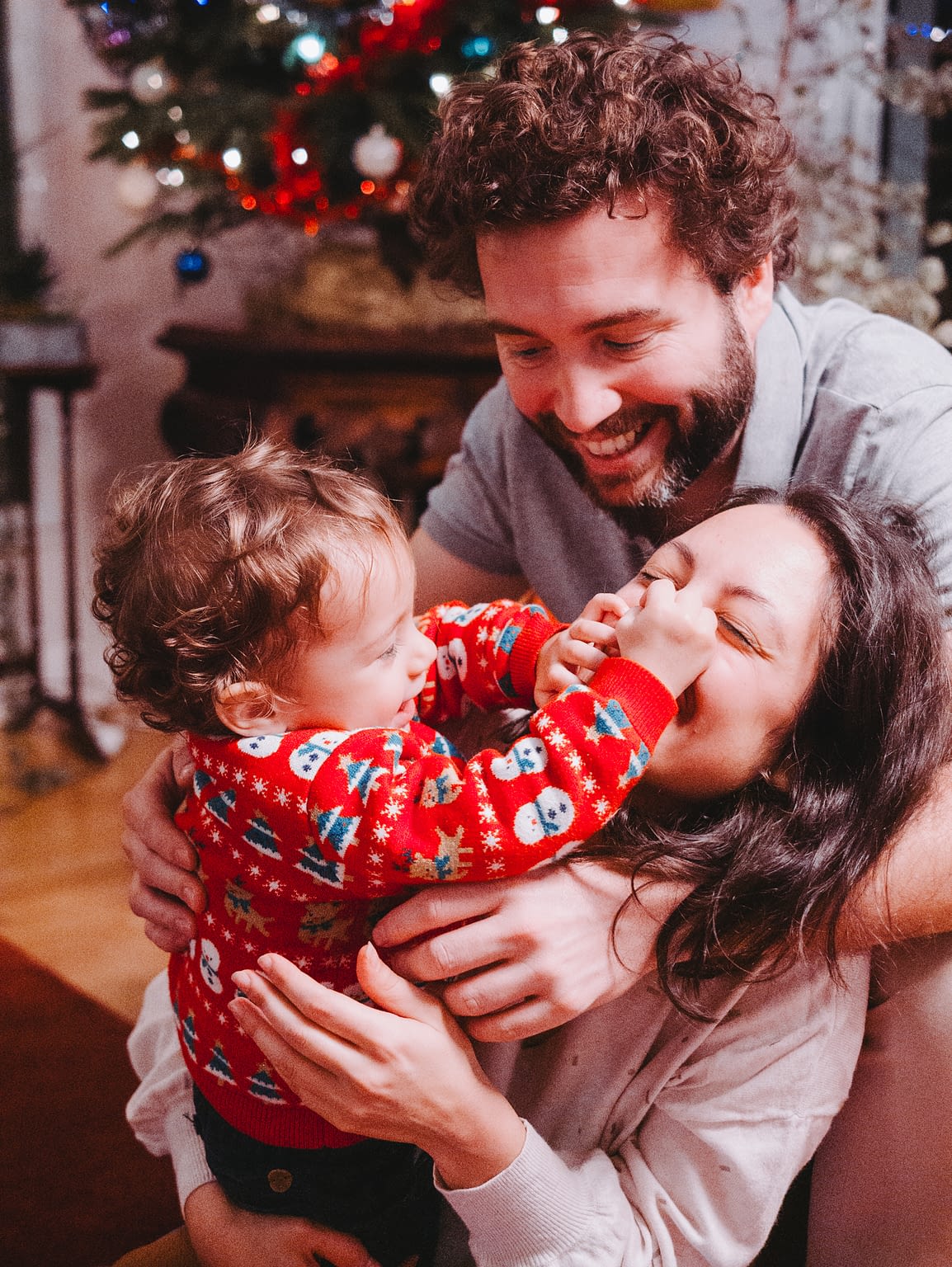 Photographie d'un couple avec leur bébé. Le petit garçon pince le nez de sa maman et tout le monde rigole