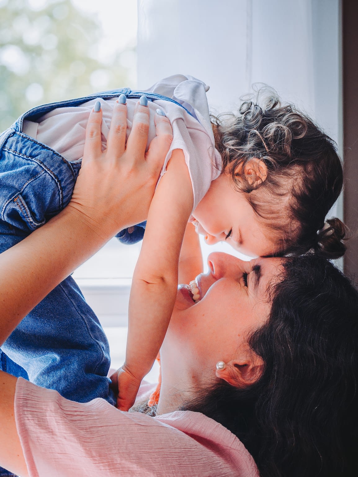 Photographie d'une maman et sa fille. La maman soulève la petite fille leurs fronts se touchent et elles sourient
