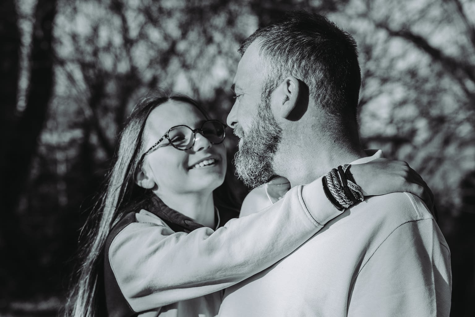 Photographie d'un papa et sa fille qui l'entoure dans ses bras. Ils se regardent avec le sourire