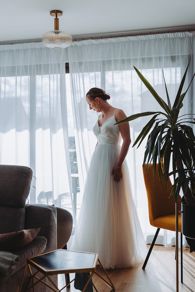 Mariée avec sa robe pendant ses essayages devant une fenêtre
